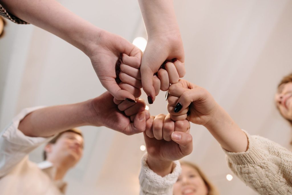 Primer plano de un grupo diverso de personas uniendo sus puños en una muestra de unidad y trabajo en equipo en un espacio cerrado.