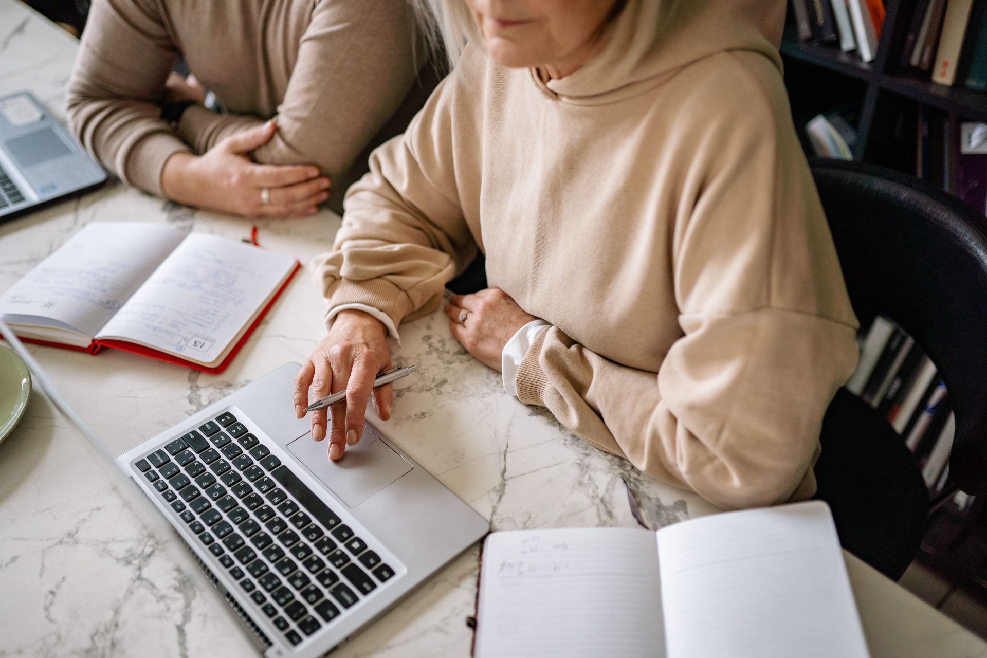 Des adultes en sweat-shirts beiges travaillent en collaboration sur des ordinateurs portables et des cahiers dans un environnement de bureau.