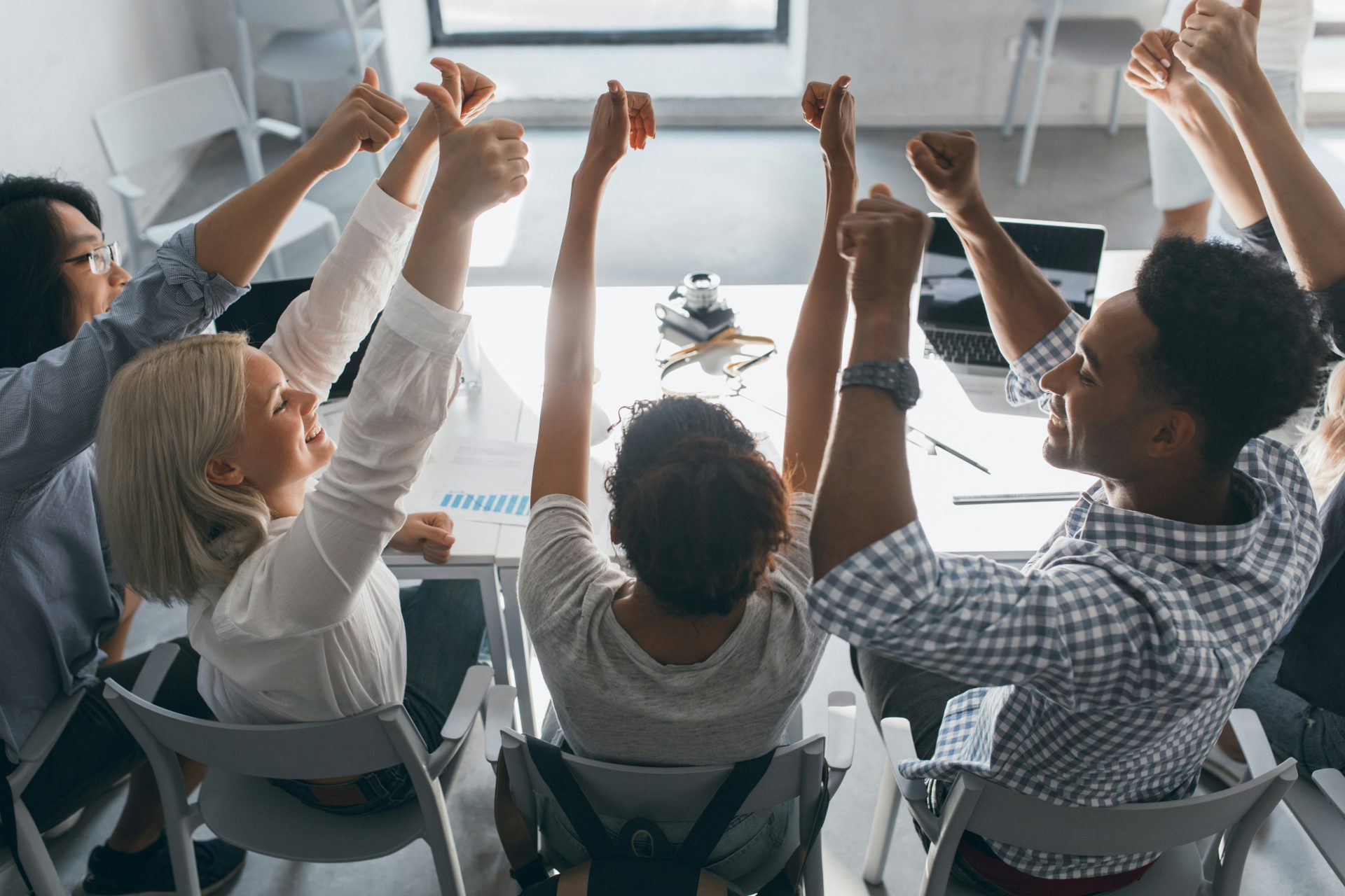 un grupo de personas sentadas a una mesa levantando la mano